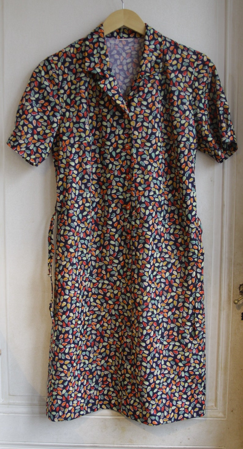 May include: A short-sleeved dress with a button-up front and a collar. The dress is made of a dark blue fabric with a pattern of small, colorful leaves.