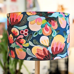 Puede incluir: Una pantalla de lámpara floral colorida con fondo azul. La pantalla presenta una variedad de flores y hojas en tonos de rosa, rojo, amarillo y verde.