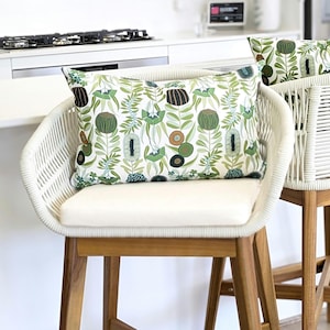 May include: Two white wicker chairs with cushions featuring a green and brown floral pattern. The chairs have wooden legs and are set against a white kitchen counter.