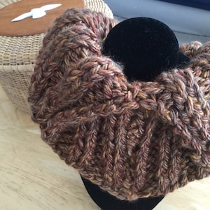 May include: A chunky knit cowl in brown, orange, and yellow yarn. The cowl is thick and warm, perfect for cold weather.