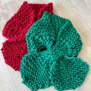 May include: Two knitted fabric squares, one red and one green, are stacked on top of each other. The fabric is a simple knit stitch.