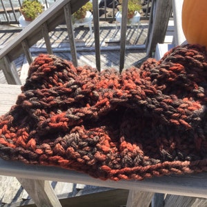 May include: A chunky knit headband in shades of brown, orange, and red. The headband is made of a soft, textured yarn and has a relaxed, slouchy fit.