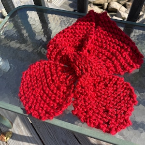 May include: A red knitted scarf with a unique, textured design. The scarf is folded in half and laid on a glass table.