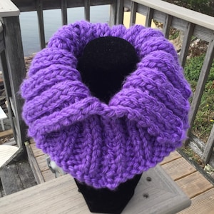 May include: A purple knitted cowl neck scarf. The scarf is made of a soft, chunky yarn and has a relaxed, slouchy fit.