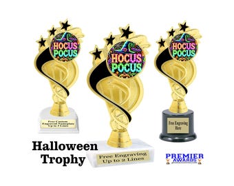 Peut inclure: Trois trophées dorés pour Halloween avec des détails noirs et des étoiles. Chaque trophée présente un emblème circulaire avec les mots "Hocus Pocus" et un chapeau de sorcière. Les socles sont blancs et noirs, avec un espace pour la gravure.