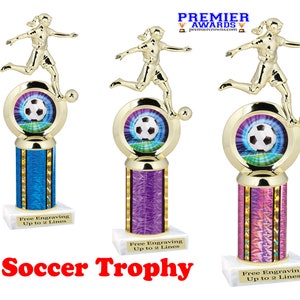 May include: Three soccer trophies with gold figures of female soccer players. Each trophy has a soccer ball in a circular frame, a column with a colorful design, and a white base with space for engraving. The text "Soccer Trophy" is at the bottom.