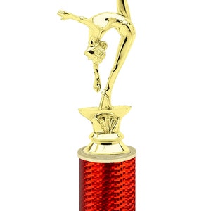 May include: Gold-colored trophy with a gymnast figurine on top. The base is red with a checkered pattern and a white base with the text "Free Engraving Up to 2 Lines".