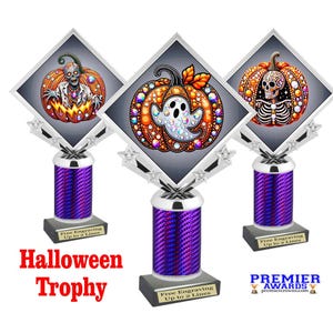 May include: Three Halloween trophies with diamond-shaped toppers featuring a zombie, ghost, and skeleton inside pumpkins. The trophies have purple columns and silver accents. The text "Halloween Trophy" is displayed in red. The trophies are for awards.