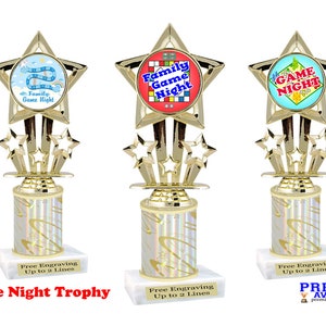 May include: Gold trophy with a star-shaped base and a white marble base. The trophy has a round, colorful image of a game board with the text "Family Game Night".