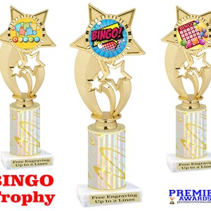 May include: Gold-colored trophy with a star-shaped base and a column with a white and gold swirl pattern. The top of the trophy features a star with a round image of a bingo card with the word "BINGO!" in a speech bubble. The base of the trophy has the text "Free Engraving Up to 2 Lines" and the words "BINGO Trophy" in red letters.
