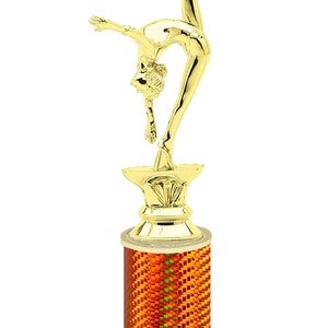 May include: Gold-colored trophy with a gymnast figure on top. The base is a cylinder with an orange and yellow pattern. The base is on a white marble base with the text "Free Engraving Up to 2 Lines".