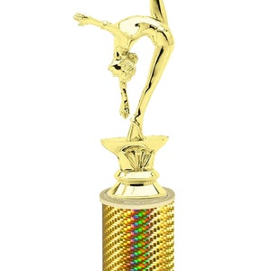May include: Gold-colored trophy with a gymnast figure on top. The base is a column with a holographic finish and a white marble base. The base has the text "Free Engraving Up to 2 Lines".