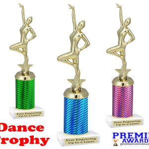 May include: Three gold-colored dancer trophies on white bases. The bases have a column with a green, blue, and pink iridescent finish. Each base has a white label that says "Free Engraving Up to 2 Lines". The text "Dance Trophy" is in red letters below the trophies. The text "PREMIER AWARDS premiercrowns.com" is in black letters below the rightmost trophy.