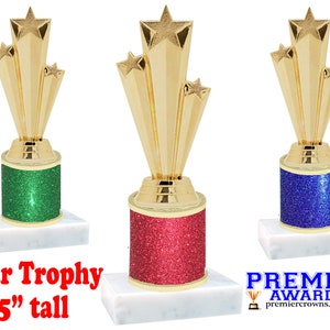 May include: Three gold star trophy awards with glitter bases in green, red, and blue. The trophies are 5 inches tall and stand on white marble bases.  "Star Trophy 5" tall" is written in red text below the trophies.  "PREMIER AWARDS premiercrowns.com" is written in blue text below the trophies.