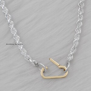 May include: A silver rope chain necklace with a gold-toned clasp. The clasp is a simple, open design.