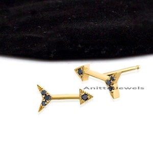 Könnte beinhalten: Ein Paar goldene Pfeilohrringe mit schwarzen Diamanten. Die Ohrringe sind klein und zart und wären ein tolles Geschenk für einen Freund oder eine geliebte Person.