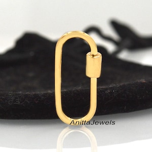 May include: A gold-colored metal clasp with an oval shape. The clasp has a small cylinder on one side.