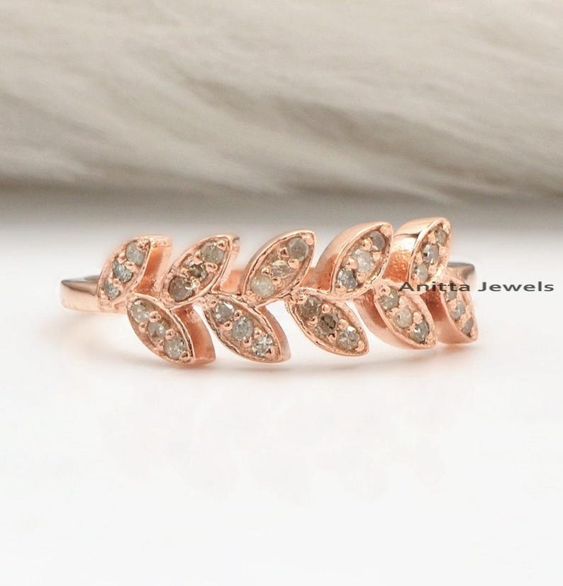 May include: Rose gold ring with a delicate leaf design set with small diamonds. The ring is a simple and elegant piece of jewelry.