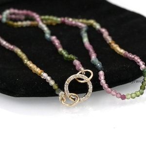 Op de afbeelding: Een veelkleurige edelsteen kralenketting met een gouden sluiting met een cirkel van kleine diamanten. De ketting ligt op een zwart fluwelen oppervlak.
