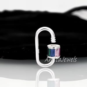 Puede incluir: Encanto de plata con una cuenta de cristal multicolor. El encanto tiene forma de gancho y tiene un pequeño bucle en la parte superior. La cuenta de cristal es un cilindro con facetas verdes, azules y rosas. El encanto está etiquetado como "Anita Jewels".