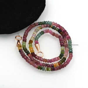 May include: A multi-colored gemstone necklace with a rose gold clasp. The necklace is made of small, round beads in shades of pink, green, and yellow.