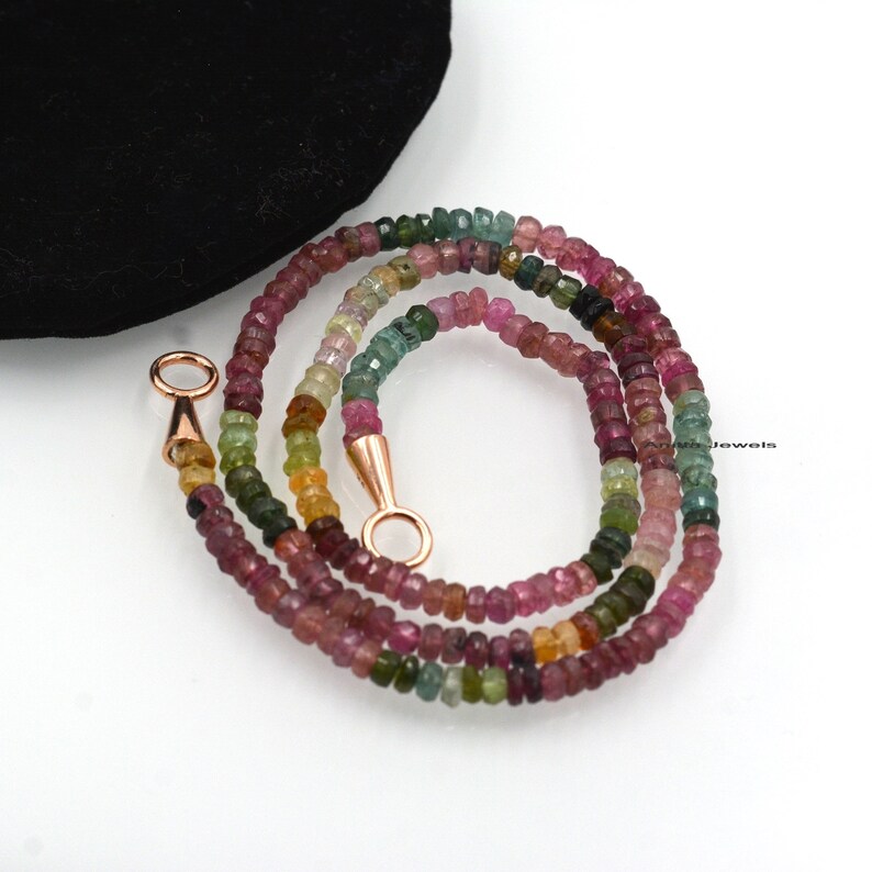 May include: A multi-colored gemstone necklace with a rose gold clasp. The necklace is made of small, round beads in shades of pink, green, and yellow.