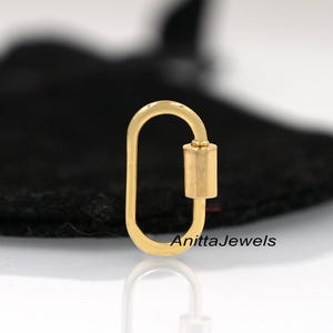 May include: Gold-toned oval-shaped lobster clasp with a cylindrical closure. The clasp is on a black surface. AnittaJewels is printed on the surface.