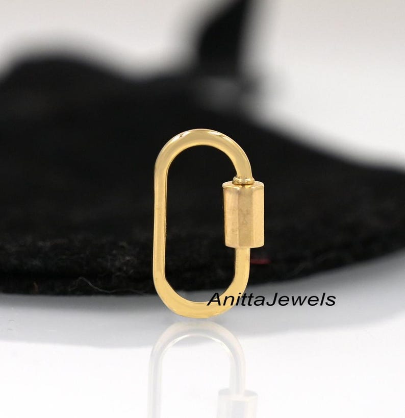 May include: Gold-toned oval-shaped lobster clasp with a cylindrical closure. The clasp is on a black surface. AnittaJewels is printed on the surface.