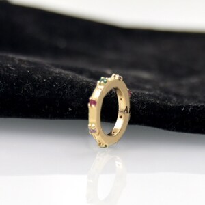 Op de afbeelding: Een gouden ring met een rij kleurrijke edelstenen rond de band.