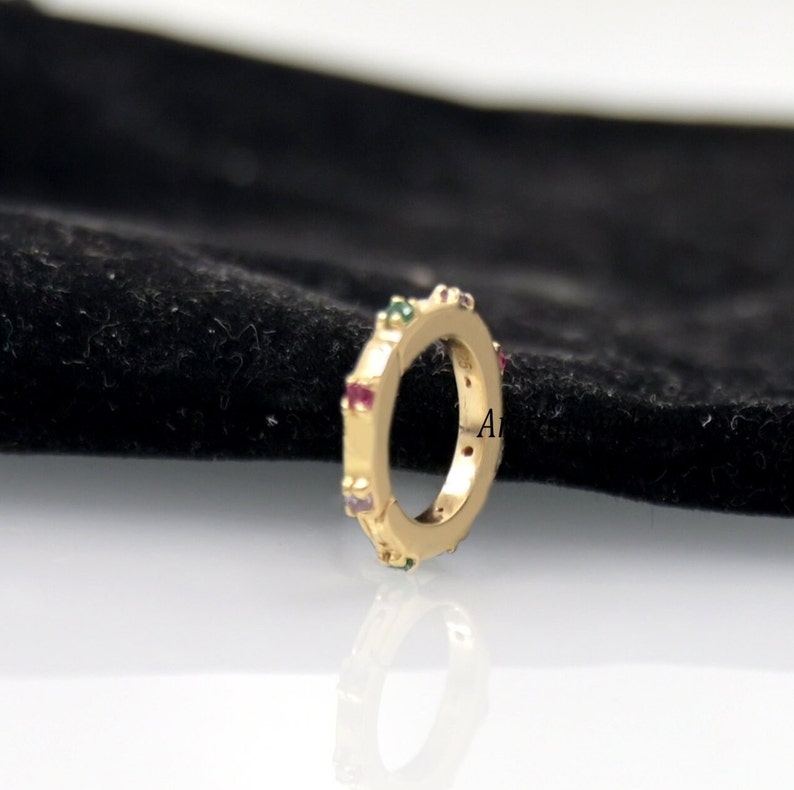Op de afbeelding: Een gouden ring met een rij kleurrijke edelstenen rond de band.