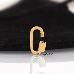 May include: Gold-toned metal clasp with a rounded oval shape. The clasp has a spring-loaded mechanism and a small, cylindrical piece on one side.