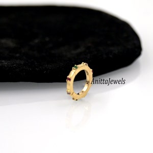 Op de afbeelding: Een gouden ring met een rij kleurrijke edelstenen. De ring ligt op een zwart fluwelen oppervlak. De tekst "Anittajewels" is zichtbaar in de afbeelding.