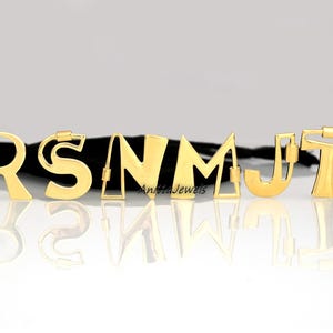 Pode incluir: Letras de metal dourado que soletram a palavra "RSNMTJ" em um fundo preto. As letras são de estilos e tamanhos diferentes.
