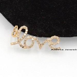 Puede incluir: Un colgante de oro en forma de la palabra "love" con pequeños diamantes transparentes engastados en el metal.