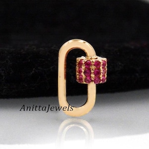 Pode incluir: Encanto dourado com uma pedra de zircônia cúbica vermelha. O encanto tem a forma de um pequeno oval com a parte superior e inferior arredondadas. O encanto é um estilo popular para a elaboração de joias.