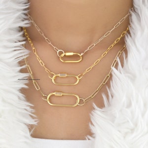 May include: Three gold chain necklaces with oval-shaped clasps. The necklaces are layered on a white fur background.