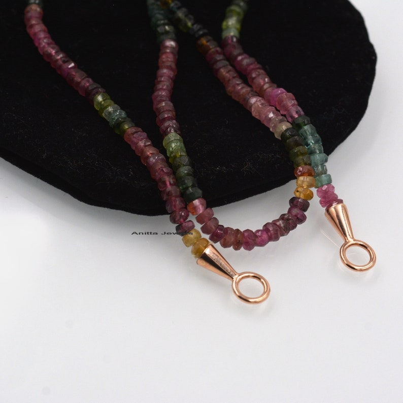 May include: A multi-colored gemstone necklace with rose gold clasps. The necklace is made of small, round beads in shades of pink, green, and yellow.