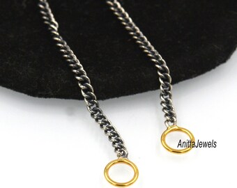 May include: A silver chain necklace with two gold jump rings. The chain is on a black surface.