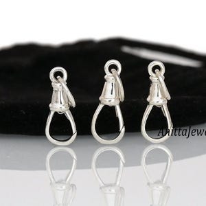 May include: Three silver-toned metal clasps with a rounded top and a hook on the bottom. The clasps are arranged in a row on a black surface.