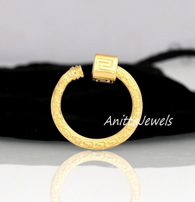 May include: A gold-colored earring with a geometric design and a square accent. The earring is a hoop shape with a screw-on closure. The text "Anita Jewels" is visible on the image.