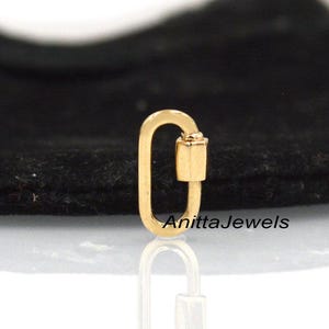 May include: Gold-toned metal clasp with a rounded oval shape and a small, cylindrical accent piece. The clasp is on a black surface. AnittaJewels is written in white text on the surface.