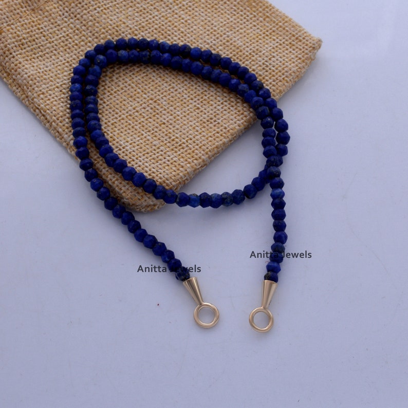 May include: A blue lapis lazuli beaded necklace with gold-toned clasps. The necklace is displayed on a burlap fabric background.