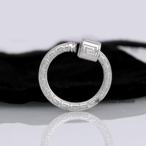 May include: A silver-colored hoop earring with a Greek key pattern. The earring features a square-shaped charm with a matching design. The earring is shown against a dark background.