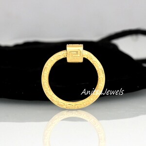 May include: A gold-colored ring with a geometric design. The ring is circular with a square accent at the top. The ring has a repeating pattern around the band. The text "Anita Jewels" is visible on the ring.
