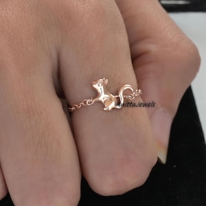 May include: A rose gold ring with a squirrel design. The squirrel is on a chain that wraps around the finger.