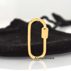 May include: Gold-toned oval-shaped lobster clasp with a cylindrical bar. The clasp is on a black velvet surface.