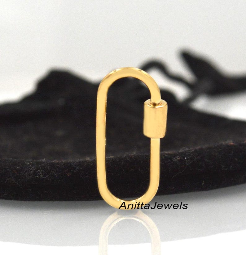 May include: Gold-toned oval-shaped lobster clasp with a cylindrical bar. The clasp is on a black velvet surface.