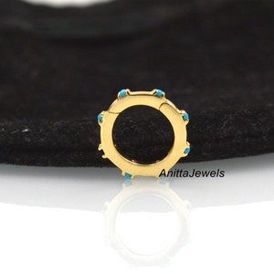 Op de afbeelding: Gouden creolen oorring met een scharnier sluiting en turquoise accenten. De oorring is op een zwarte achtergrond.