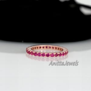 May include: Rose gold eternity ring with vibrant red gemstones. The ring features a continuous line of round-cut stones, creating a full circle of color. The ring is from Anitta Jewels.