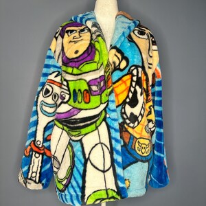 May include: A plush, hooded robe featuring colorful cartoon character designs. The robe showcases Buzz Lightyear, Woody, and other characters against a blue and white striped background. The robe is displayed on a mannequin.